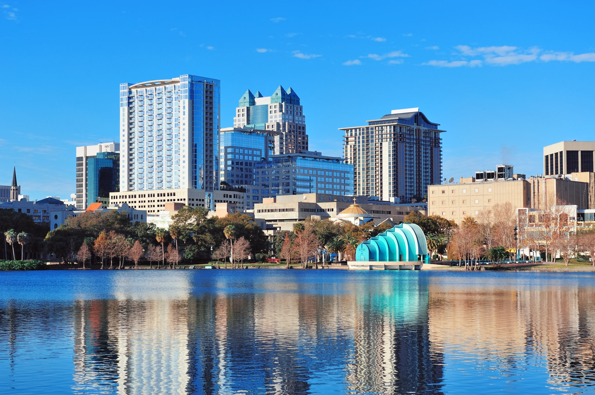Alt-Text: Der Lake Eola in Orlando am Morgen mit spiegelglattem Wasser, modernen Wolkenkratzern und strahlend blauem Himmel.