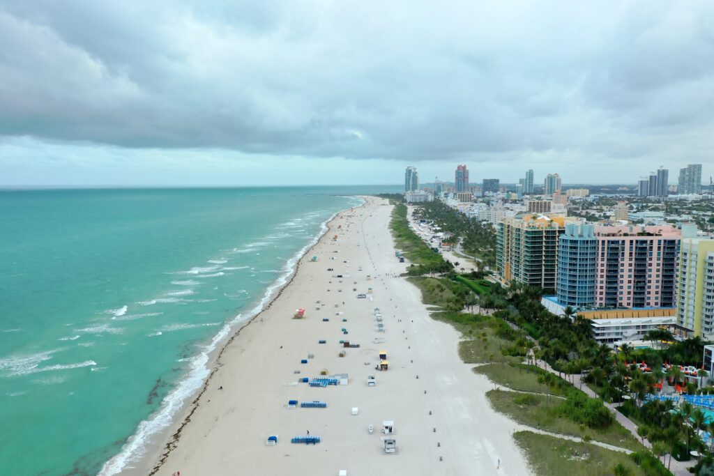 Luftaufnahme von Miami Beach mit dem türkisfarbenen Ozean und den ikonischen Art-Déco-Gebäuden auf der rechten Seite.