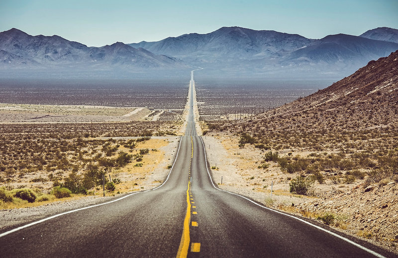 Eine einsame Straße im Westen der USA, die am Horizont in der unendlichen Weite verschwindet.
